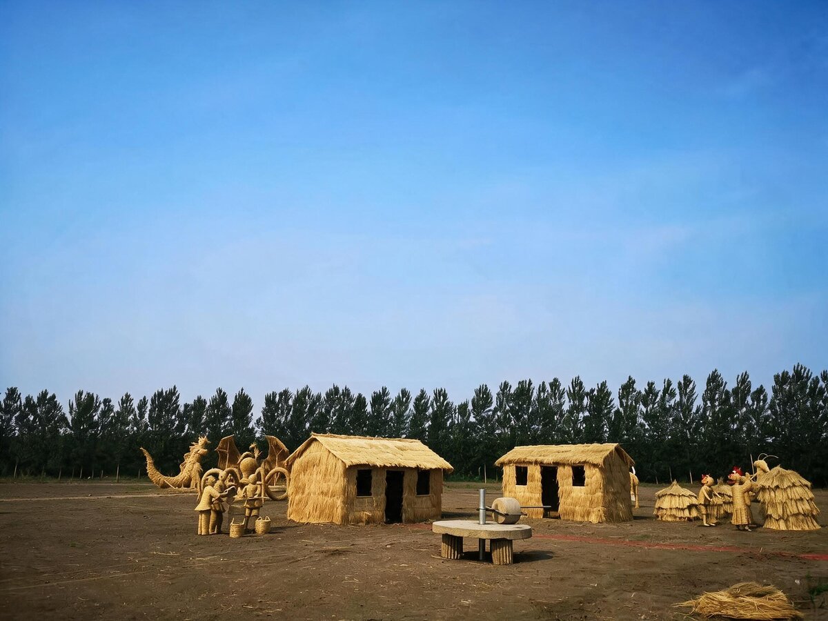 Straw‑built houses and character sculptures, large outdoor straw art landscape